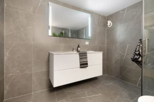 Baie modernă cu plăci ceramice mari, de culoare deschisă, și duș walk-in cu rigolă liniară