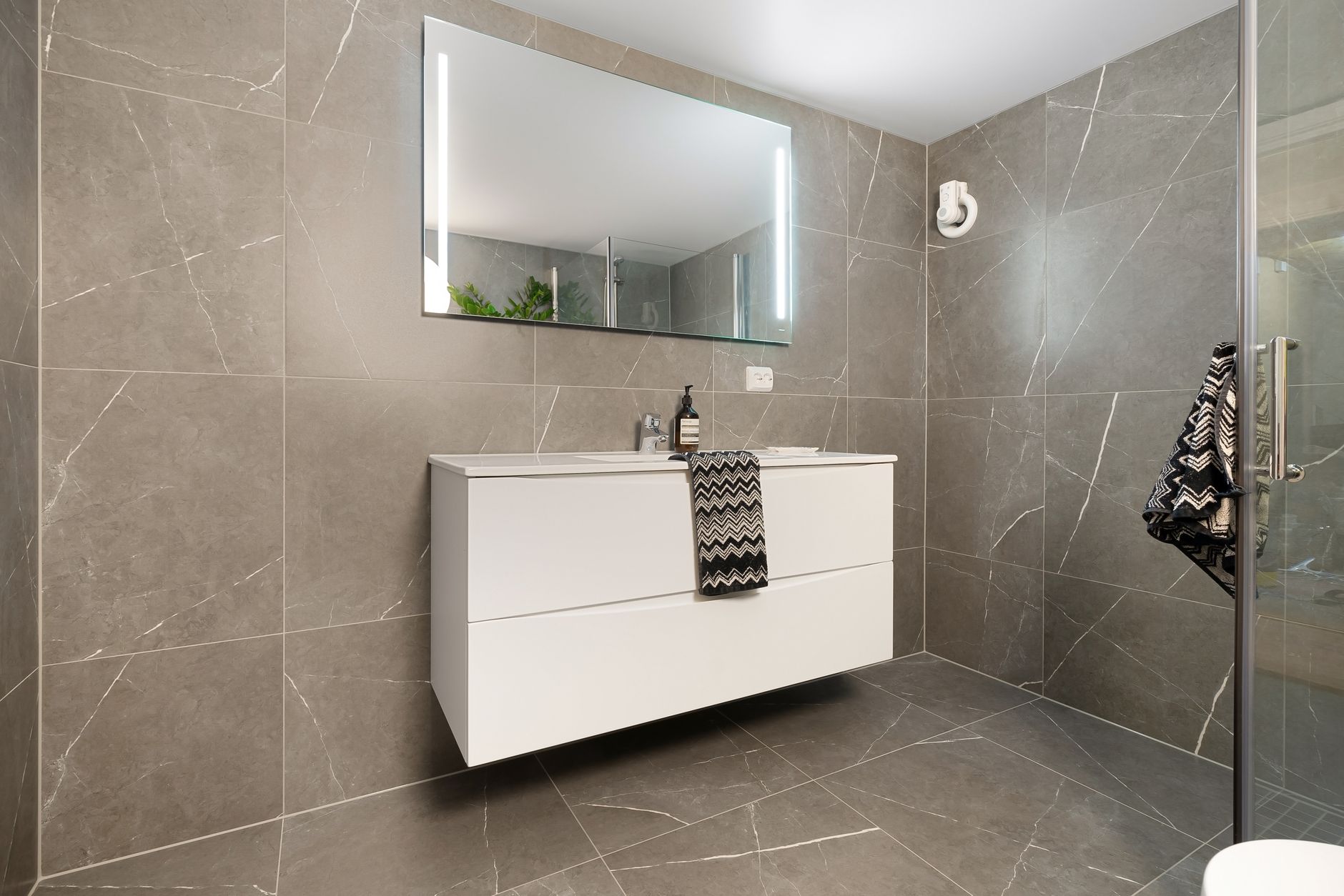 Baie modernă cu plăci ceramice mari, de culoare deschisă, și duș walk-in cu rigolă liniară